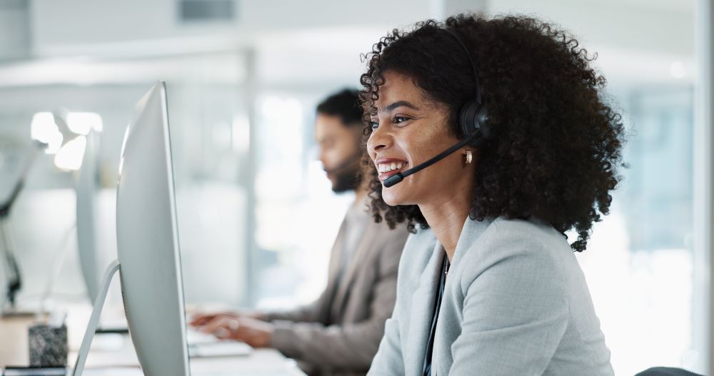 Healthcare professional with headset, smiling, looking at screen.